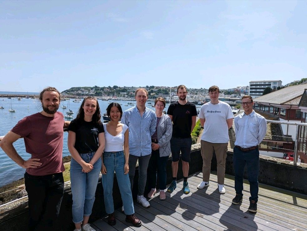 Multiple people from Exeter photonics standing in front of a seaside harbour on the balcony of Effect Photonics Brixham